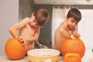 The two boys are making lanterns out of pumpkins by themselves in preparation for the upcoming Halloween party.